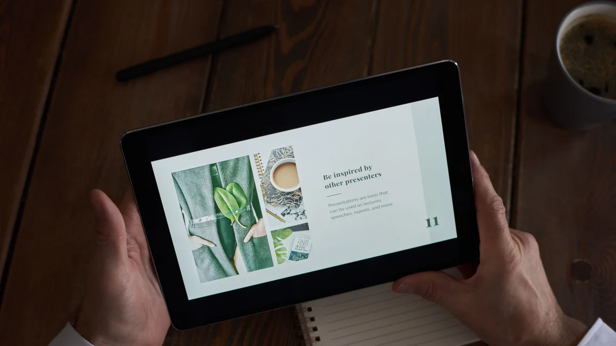 Hands holding a tablet displaying a presentation on a wooden desk