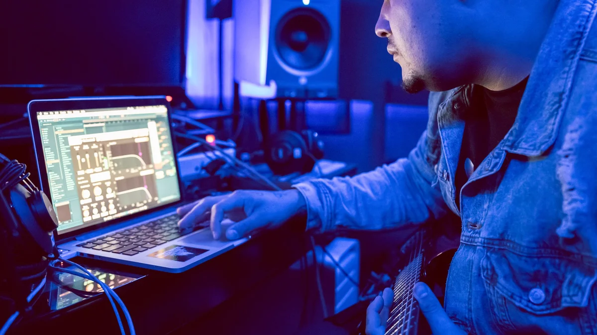 Musicien travaillant sur un ordinateur portable dans un home studio éclairé en bleu